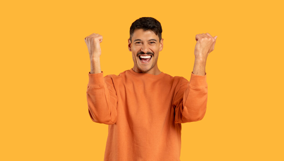 A man wearing an orange shirt is raising his hands up in the air in a gesture of celebration or victory.