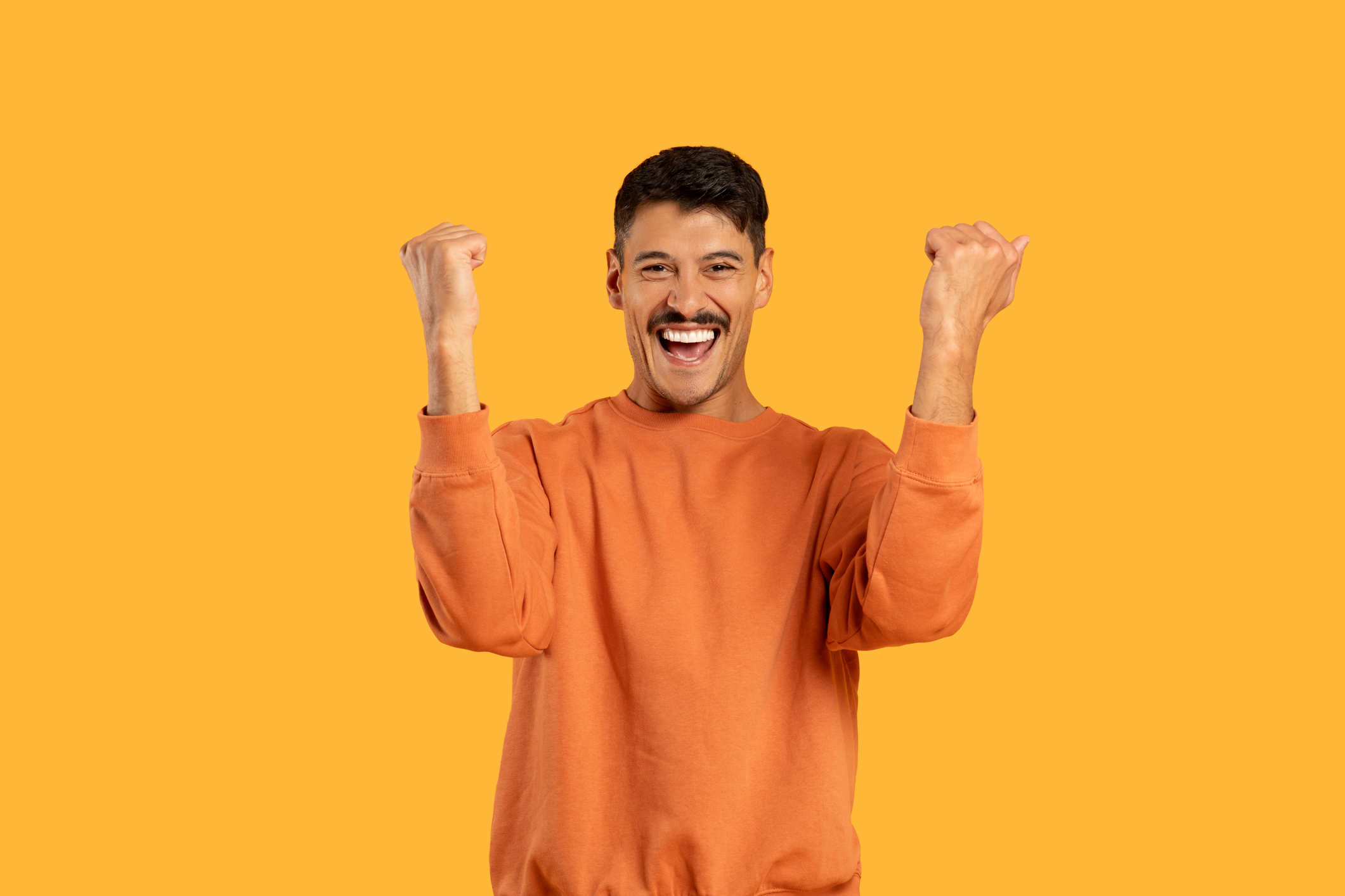 A man wearing an orange shirt is raising his hands up in the air in a gesture of celebration or victory.