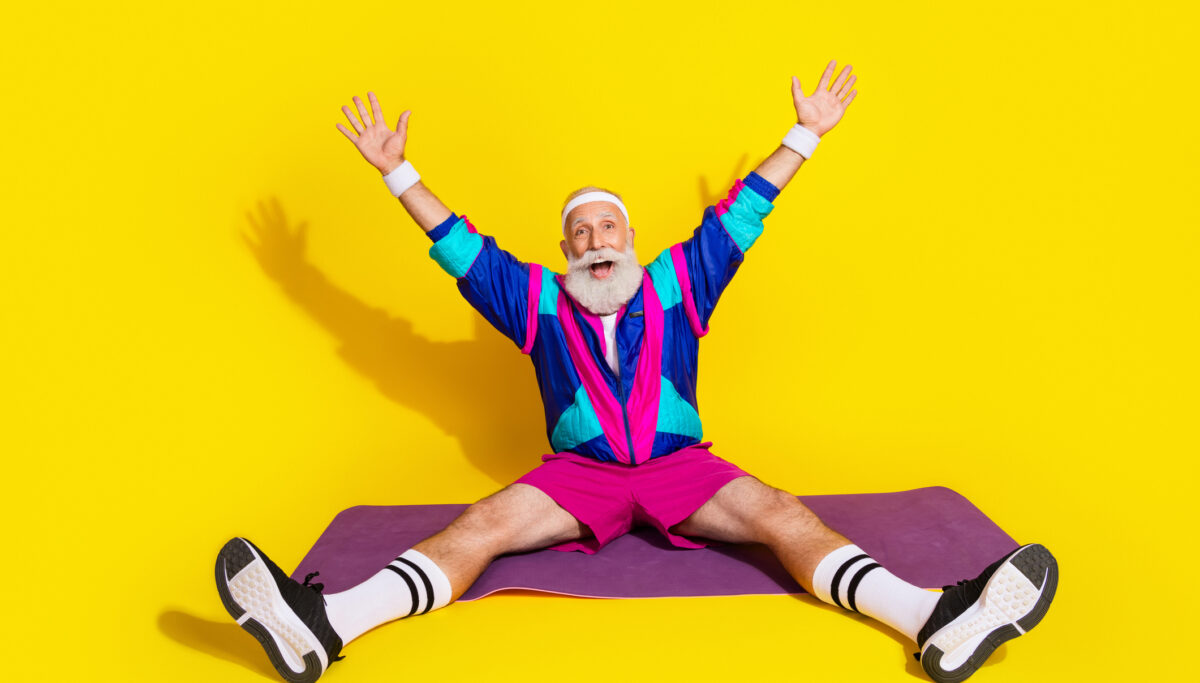 Full body portrait of eccentric aged man sit fitness carpet workout retro sportswear isolated on yellow color background.