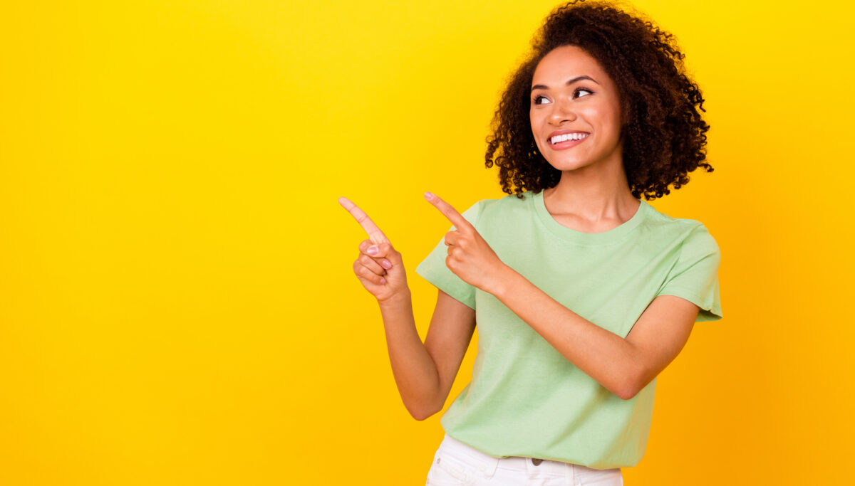 Photo of woman smiling and pointing upwards on a yellow background.