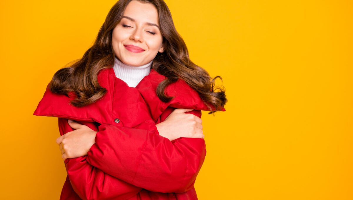 Photo of charming lady traveler enjoy warm weather hugging shoulders, eyes closed overjoyed wear red warm winter outerwear coat isolated yellow color background