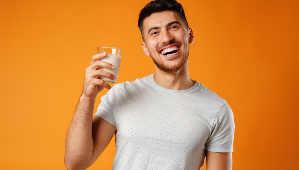 Happy smiling man holding milk against orange background close up