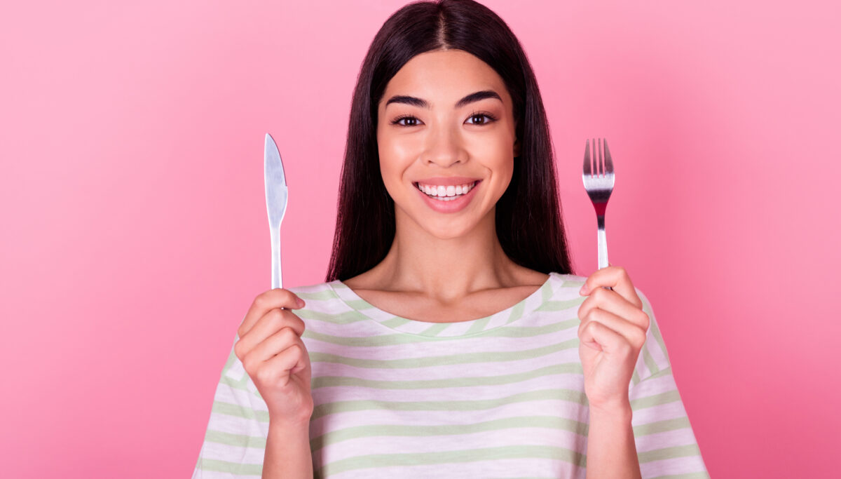 Happy woman holding fork and knife on a pink background