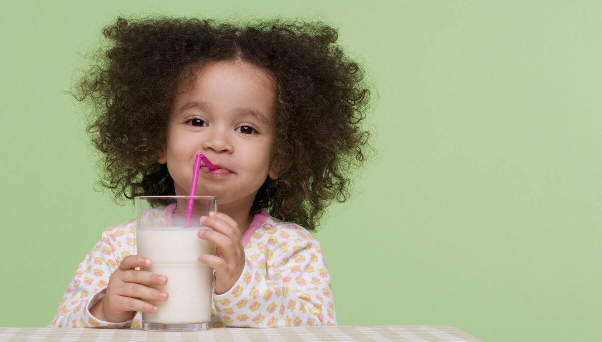 Little girl drinking milk at table, green background.