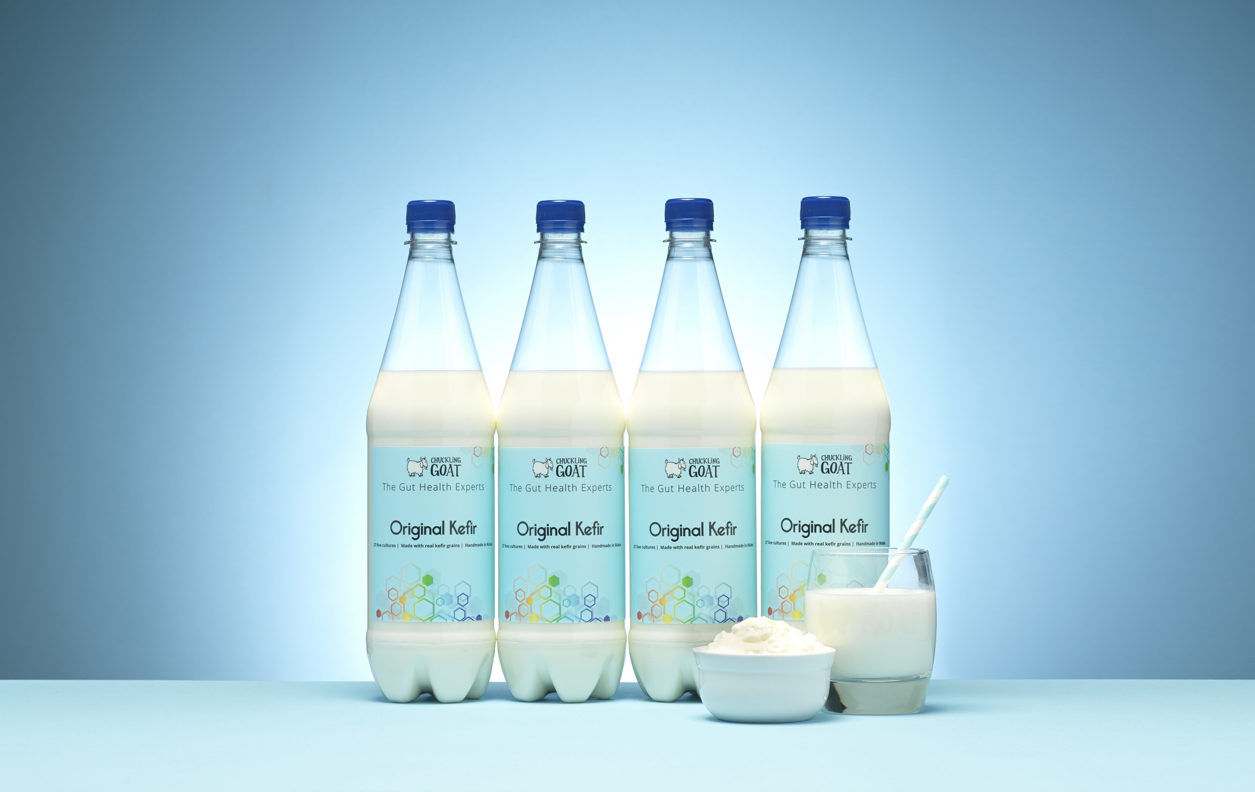 Four bottles of Chuckling Goat Original Kefir on a blue background.