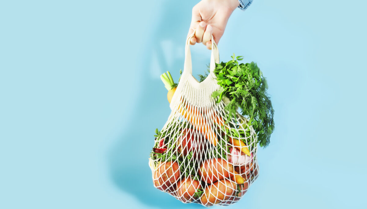 Mesh bag filled with whole, plant foods on a blue background.