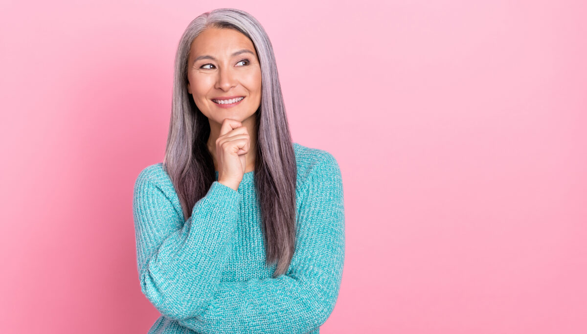 Photo of cheerful mature woman thinking on a pink background.