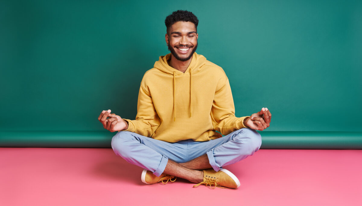 Happy man meditating while sitting against colorful background