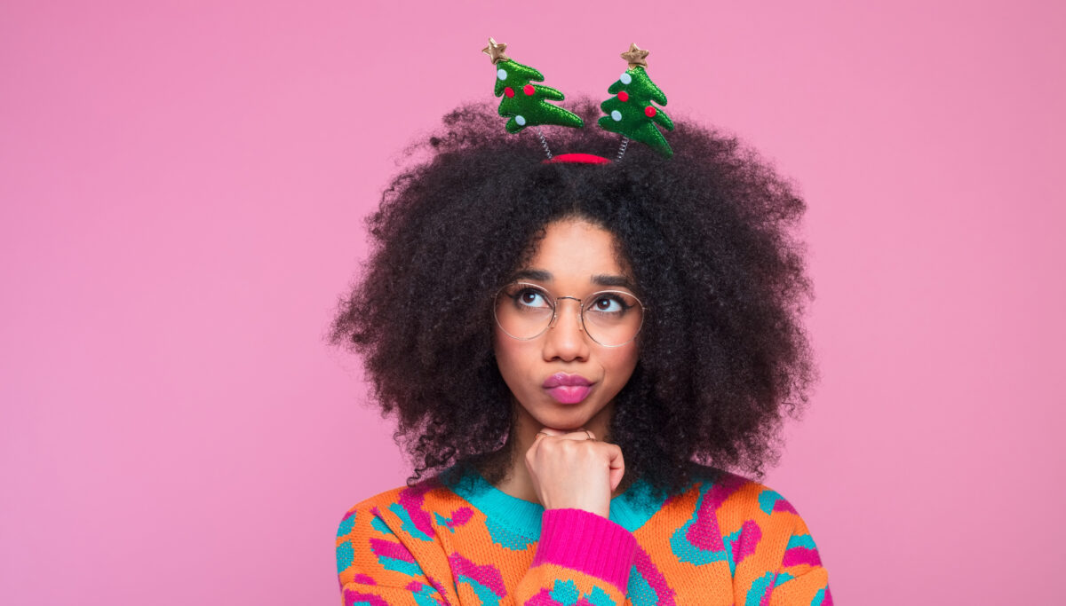 Woman looking thoughtful in a festive outfit on a pink coloured background.