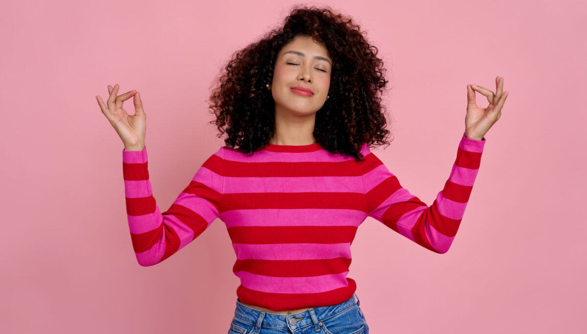 Woman looking peaceful and happy with eyes closed doing meditation on a pink background.