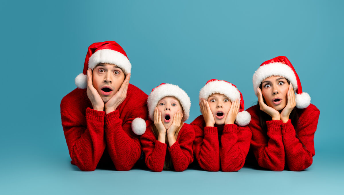 A family wearing Santa hats and red sweaters showcases exaggerated surprised expressions in celebration of the Christmas season.