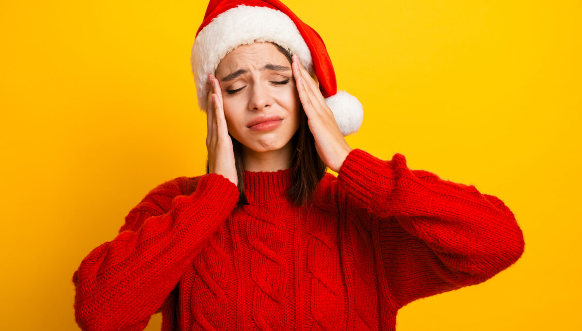 A woman in a red jumper and santa hat feeling stressed on a yellow background
