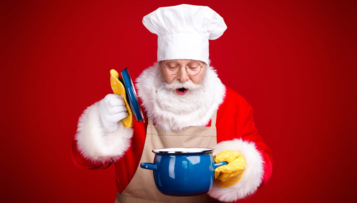A cheerful Santa in a chef hat and apron cooks a festive meal, holding colorful plates over a blue pot against a bright red background creating a warm holiday mood.