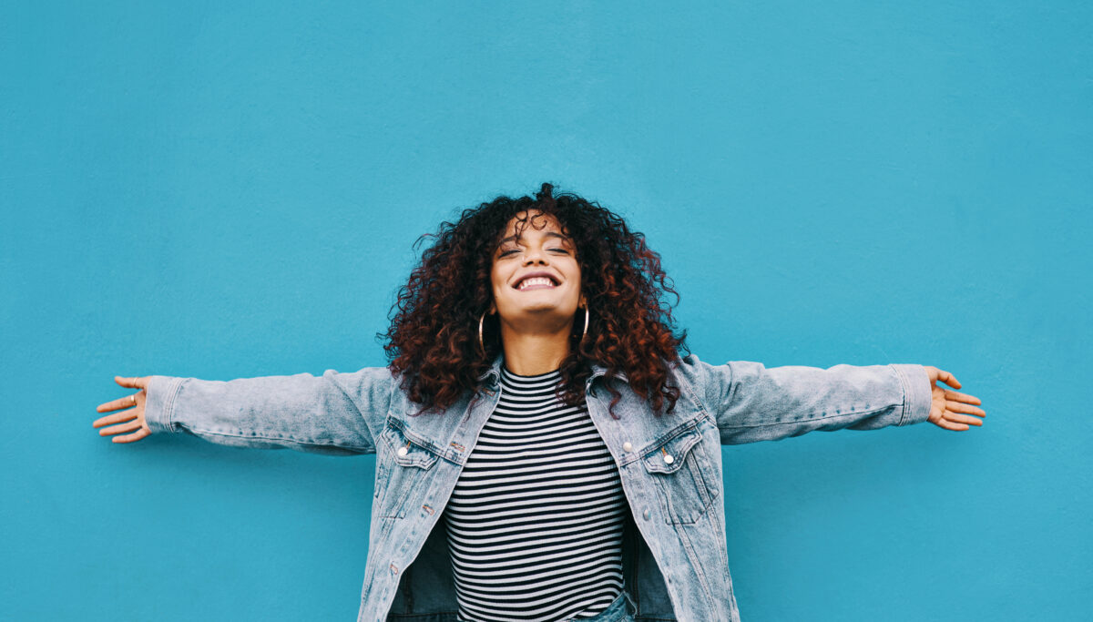 Cropped portrait of an attractive young woman standing with her arms outstretched against a blue background