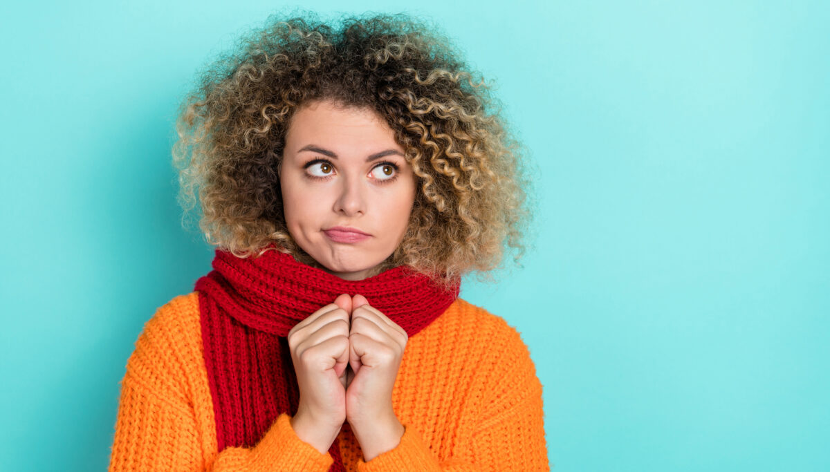 Sad and tired woman wearing a jumper and scarf on a blue background.