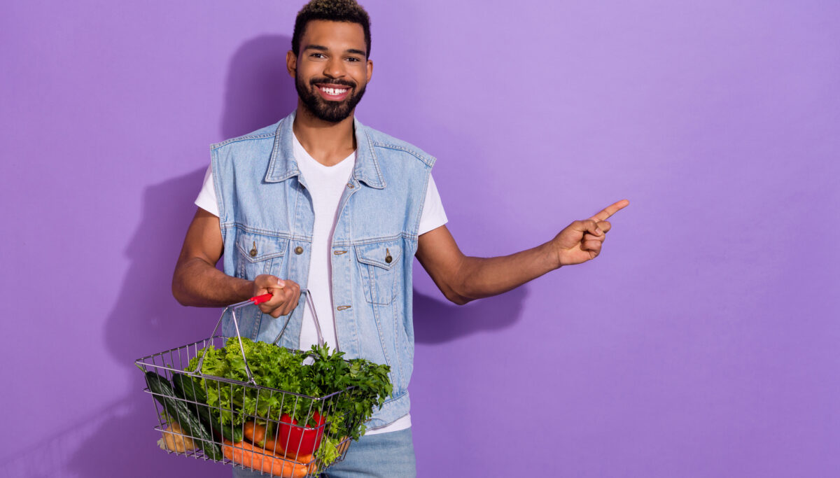 Photo of man wear jeans waistcoat pointing empty space buying fresh veggies isolated violet color background.