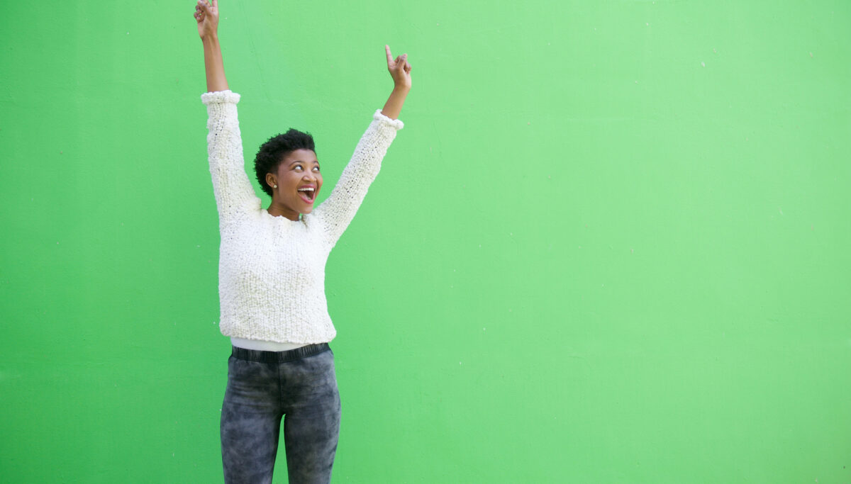 Portrait of a happy young african american woman cheering with arms raised