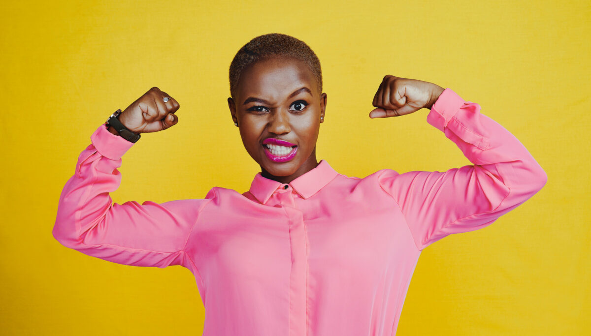 Portrait of an attractive young woman flexing her biceps against a yellow background