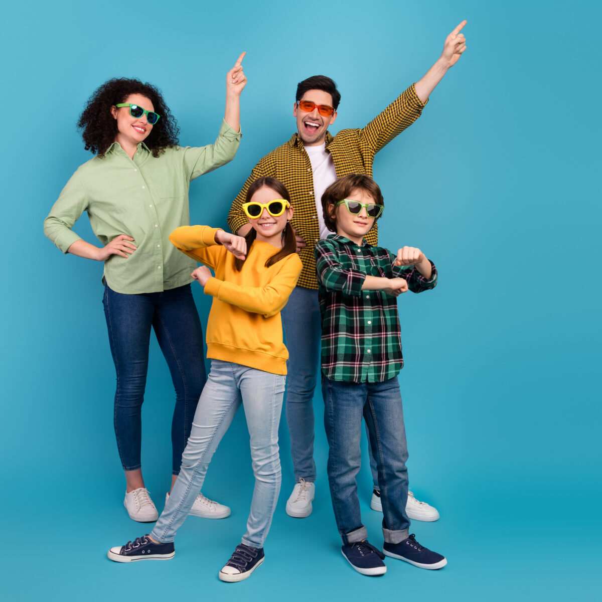 Happy young family posing playfully against blue background, expressing joy and togetherness with stylish outfits and gestures