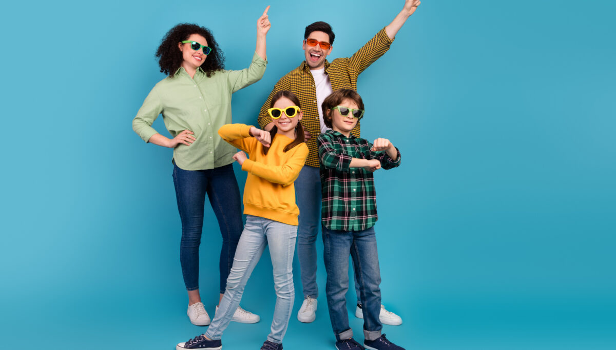 Happy young family posing playfully against blue background, expressing joy and togetherness with stylish outfits and gestures