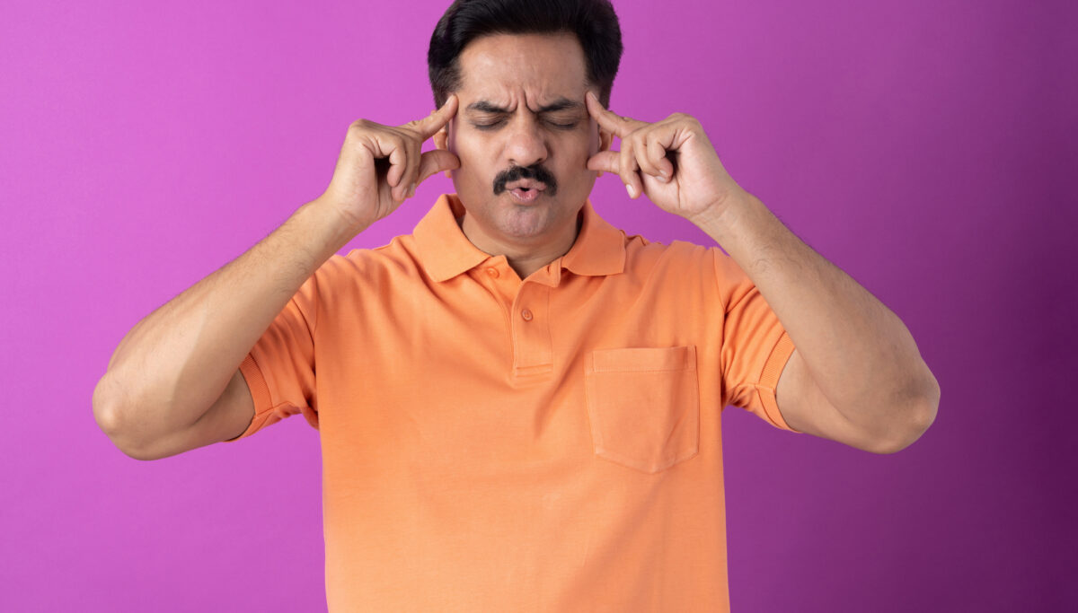 Man focusing, touching sides of head with hands, on isolated purple background